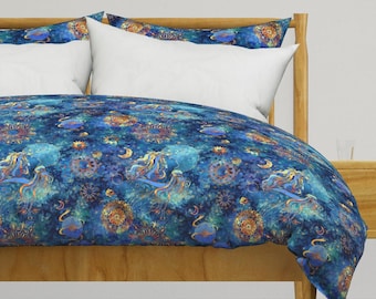 Könnte beinhalten: Ein blauer und goldener Bettbezug mit einem himmlischen Muster mit Sternen, Monden und wirbelnden Designs. Der Bettbezug befindet sich auf einem Holzbettgestell mit weißen Kissen.