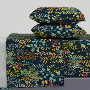 Puede incluir: Un juego de cama azul oscuro con un patrón floral que presenta hojas amarillas, verdes y naranjas y pájaros pequeños. El juego incluye una sábana ajustable, una sábana plana y dos fundas de almohada.