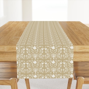 May include: A beige table runner with a white pattern of menorahs, doves, and wine glasses. The pattern is repeated throughout the runner.