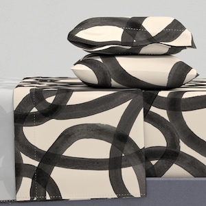 May include: A set of cream-colored bedding with a black abstract pattern of overlapping circles. The set includes a fitted sheet, flat sheet, and two pillowcases.