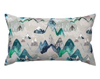 May include: A rectangular throw pillow with a light gray background and a repeating pattern of blue, green, and white mountains. The mountains are stylized and have a watercolor effect.