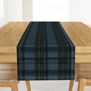 May include: A blue and green plaid table runner with a white border. The runner is on a wooden table.