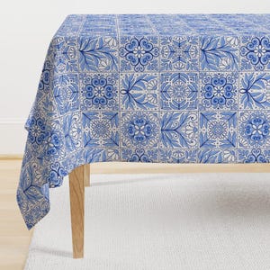 May include: A white tablecloth with a blue and white tile pattern. The tablecloth is draped over a wooden table.