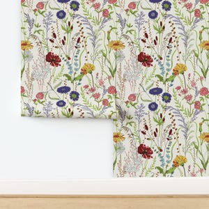 May include: Wallpaper featuring a repeating botanical pattern on a light cream background. The design includes illustrations of wildflowers in shades of red, yellow, blue, purple, and green, with various stems, leaves, and small floral clusters.