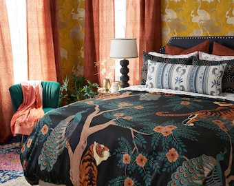 May include: A black duvet cover with a tiger and peacock design. The duvet cover is on a bed with a variety of pillows, including a blue and white striped pillow. The bed is in a bedroom with orange curtains and a yellow wallpaper with a crane pattern.