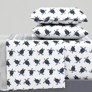 May include: A white bed sheet with a blue sea turtle pattern. The sheet is folded and stacked on top of two matching pillowcases.