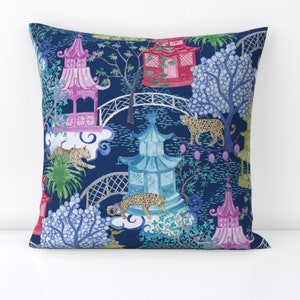 May include: Decorative square pillow with a navy blue background featuring a whimsical Asian-inspired design. The pattern includes pagodas in pink, blue, and red, along with leopards, bridges, and trees. The pillow is a square shape.