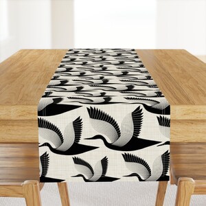 May include: Black and white table runner featuring a geometric pattern of stylised birds. The birds are flying in a repeating pattern on a cream-coloured background.