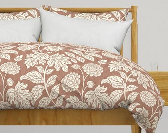 May include: A blush pink duvet cover with a white floral pattern. The duvet cover is on a bed with a wooden headboard and white pillows.