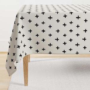 Puede incluir: Un mantel blanco con un patrón de signos más negros. El mantel está sobre una mesa de madera con una alfombra blanca debajo.