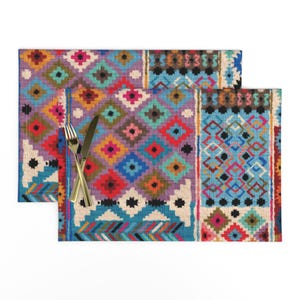 May include: Two colorful patterned placemats with a geometric design in shades of blue, red, pink, yellow, and green. The placemats are made of a woven fabric and have a fringed edge.