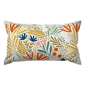 May include: Rectangular decorative pillow with a floral pattern. The pillow features a white background with a repeating design of orange, yellow, blue, and pink flowers and leaves. The pillow is designed for home decor.