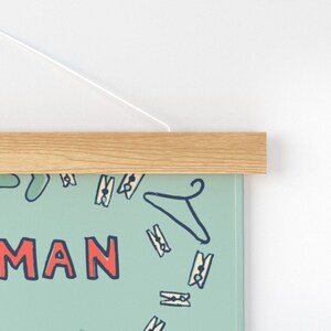 Pu&ograve; includere: Una stampa su tela blu chiaro con una cornice in legno bianco. La stampa presenta un motivo ripetitivo di mollette da bucato e grucce. Il testo "HUMAN" &egrave; scritto in rosso nella parte inferiore della stampa.