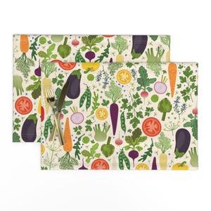 May include: A set of two placemats with a colorful pattern of vegetables, including carrots, tomatoes, onions, eggplant, and artichokes on a cream background.