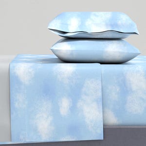 Pode incluir: Um conjunto de roupa de cama azul e branco com um padrão de nuvens. O conjunto inclui um lençol de elástico, um lençol plano e duas fronhas.