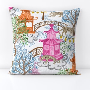 May include: White throw pillow with a colorful pattern of pink and orange pagodas, green trees, and leopard print animals. The pattern is repeated throughout the pillow.