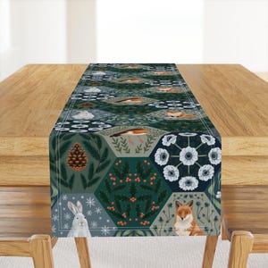 May include: A green, blue, and white table runner with a geometric pattern featuring a fox, a rabbit, a bird, pine cones, and snowflakes.