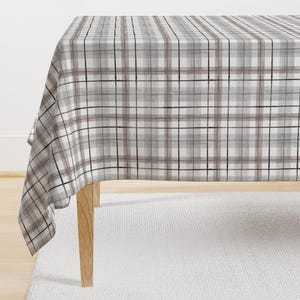 May include: A white tablecloth with a brown and black plaid pattern. The tablecloth is draped over a table with wooden legs.