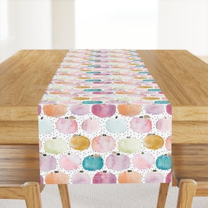 May include: A white table runner with a repeating pattern of colorful watercolor pumpkins on a white background with black polka dots.
