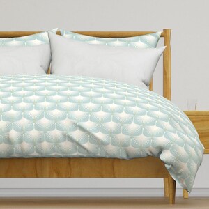 May include: A light blue duvet cover with a white geometric pattern of sunbursts. The duvet cover is on a wooden bed frame with two white pillows.
