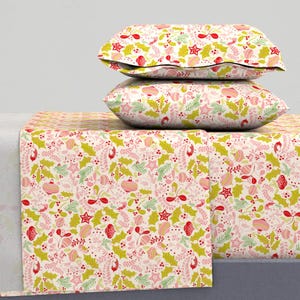 May include: A bedding set featuring a festive Christmas pattern. The set includes two pillows and a sheet, all adorned with a repeating design of red, pink, and green holiday elements like stars, ornaments, and holly leaves on a white background.