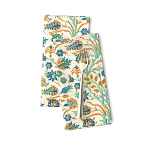 May include: Two white fabric napkins with a colorful floral pattern. The pattern features orange, blue, and green flowers and leaves on a white background.