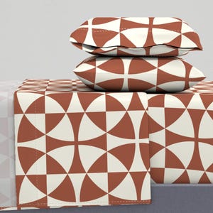 May include: A set of rust-coloured bedding with a geometric pattern of white circles and semi-circles. The set includes a fitted sheet, flat sheet, and two pillowcases.