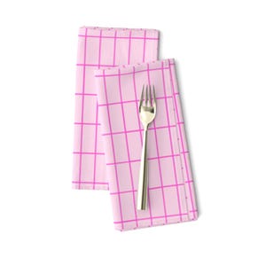 Op de afbeelding: Twee roze servetten met een wit rasterpatroon. De servetten zijn gevouwen en een zilveren vork ligt erop.