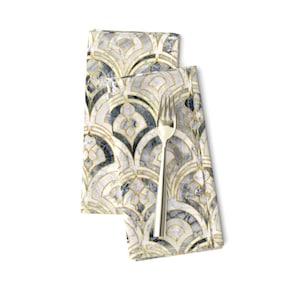 May include: Two folded cloth napkins with a gold, white, and navy blue art deco pattern. A silver fork rests on top of the napkins. The napkins have a marble-like appearance.