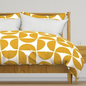 Op de afbeelding: Een witte dekbedovertrek met een geometrisch patroon van mosterdgele halve cirkels. De dekbedovertrek ligt op een bed met een houten hoofdbord en twee witte kussens.