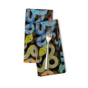 May include: Two black fabric napkins with a colorful pattern of stylized snakes on a black background. The snakes are yellow, green, blue, and orange.