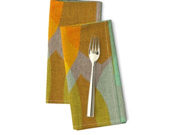 Pode incluir: Duas toalhas de mesa dobradas com um padrão geométrico em tons de amarelo, laranja, verde e castanho. As toalhas de mesa têm uma textura subtil e uma borda verde claro.