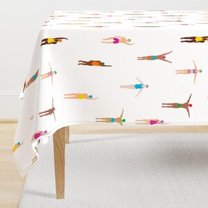 May include: White tablecloth featuring a repeating pattern of swimmers in various positions. The swimmers are depicted in a minimalist style with colorful swim caps and swimsuits. The table is set on a light-colored rug.