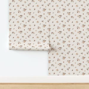 Puede incluir: Un rollo de papel pintado con un fondo crema y un patrón repetido de pequeños ramos florales dispersos en tonos marrón, melocotón y gris. El papel pintado está parcialmente desenrollado, revelando el diseño.