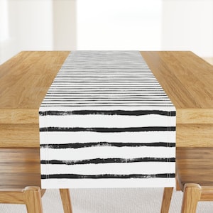May include: Black and white striped table runner with a brushstroke pattern. The runner is on a wooden table.