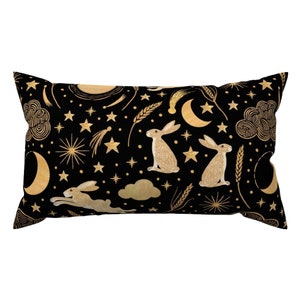 May include: A black lumbar pillow with a gold pattern of stars, moons, wheat, and rabbits. The pattern is repeated throughout the pillow.