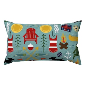 May include: A teal blue pillow with a repeating pattern of summer camp and lake icons. The icons include a red and white swimsuit, a red Adirondack chair, a yellow canoe, a yellow sun, a green pine tree, a red and white fishing bobber, a black dog, a blue anchor, a yellow campfire, and a blue and white rope knot.