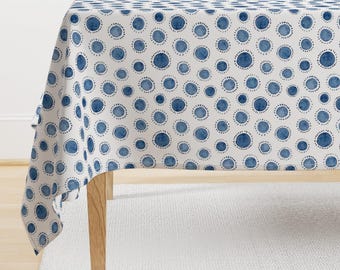 May include: A white tablecloth with a blue watercolor polka dot pattern. The tablecloth is draped over a wooden table.