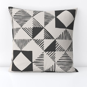 May include: A black and white geometric patterned throw pillow with a cream background. The pattern features squares, triangles, and lines.