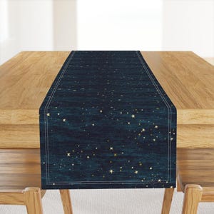 May include: A dark blue table runner with a celestial design featuring gold stars. The runner has a textured appearance and a thin, white border. It is displayed on a wooden table, adding a touch of elegance to any dining setting.