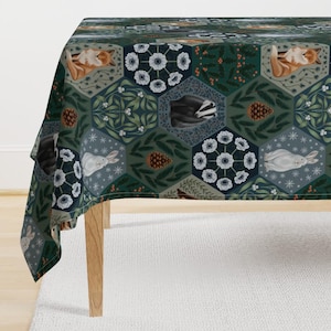 May include: A blue and green tablecloth with a repeating pattern of woodland animals, flowers, and pine cones. The animals include a fox, a badger, and a rabbit. The flowers are white with yellow centers. The pine cones are brown.