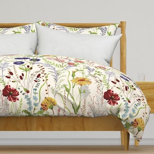 May include: A duvet cover and matching pillowcases featuring a cream-colored background with a botanical print of wildflowers. The pattern includes red poppies, yellow daisies, blue cornflowers, and various green grasses and stems.
