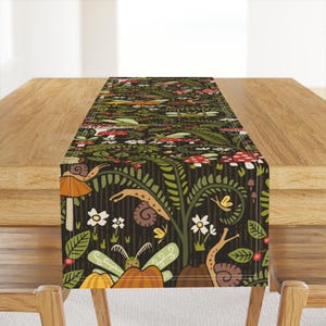 May include: A green, brown and red table runner with a whimsical forest scene featuring mushrooms, snails and dragonflies. The runner has a dark background with a striped pattern.