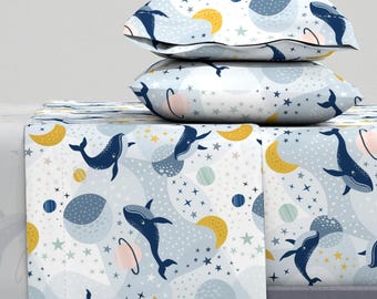 May include: A white bedding set with a blue whale and star pattern. The set includes a fitted sheet, flat sheet, and two pillowcases.