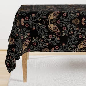 May include: A black tablecloth featuring a repeating pattern of tan and muted red moths, skulls, and floral vines. The design includes stylized insects with skull-like markings on their bodies, interspersed with small flowers and leafy branches.