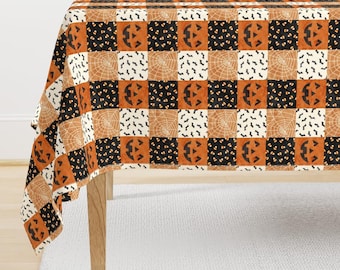 Puede incluir: Un mantel rectangular con un patrón de mosaico repetitivo de cuadrados con temática de Halloween. El diseño incluye caras de calabaza naranjas, cuadrados negros con caramelos, cuadrados blancos con murciélagos negros y telarañas color canela.