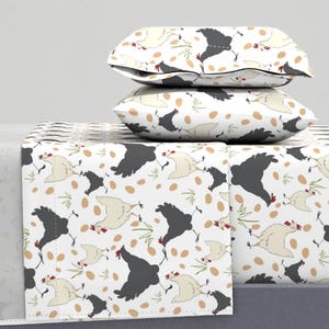 Puede incluir: Bedding blanco con un patrón repetido de pollos negros y huevos marrones. El juego de cama incluye una sábana bajera, una sábana plana y dos fundas de almohada.