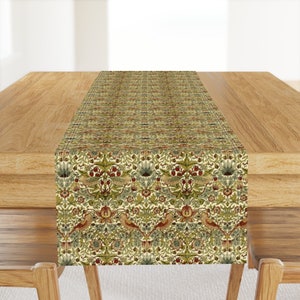 May include: A green and cream table runner with a repeating pattern of birds, flowers, and leaves. The runner is on a wooden table.