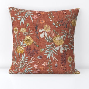 May include: A rust-colored throw pillow with a floral pattern featuring blue, green, and yellow flowers. The pillow has a subtle linen texture.