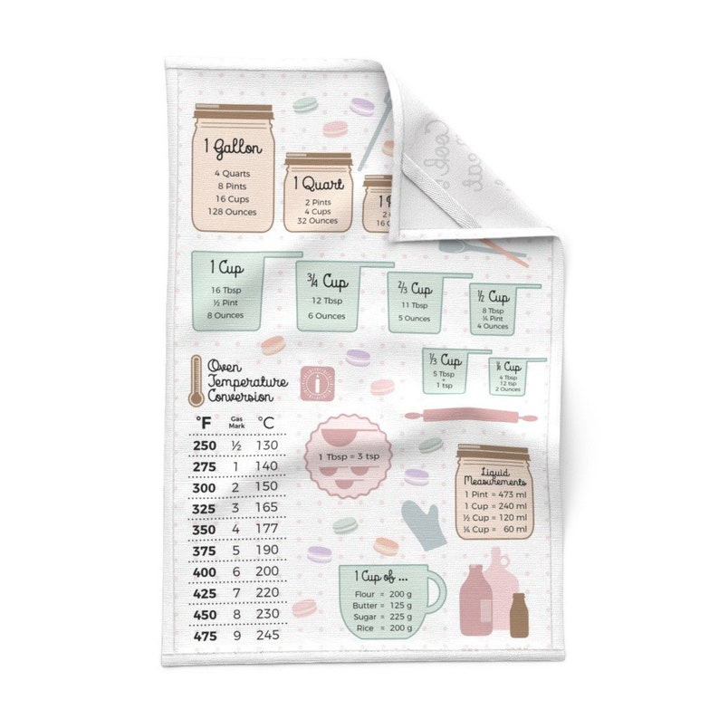 May include: A white kitchen towel with a colorful design featuring macarons, measuring cups, and a chart for converting oven temperatures from Fahrenheit to Celsius. The text on the towel includes "1 Gallon", "1 Quart", "1 Cup", "3/4 Cup", "1/2 Cup", "1/4 Cup", "Oven Temperature Conversion", "1 Tbsp = 3 tsp", "Liquid Measurements", "1 Cup of...", "Flour = 200 g", "Butter = 125 g", "Sugar = 225 g", "Rice = 200 g".